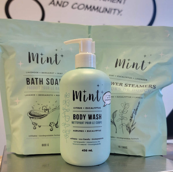 Mint branded body wash bottle with bath soap and steamers in the background.